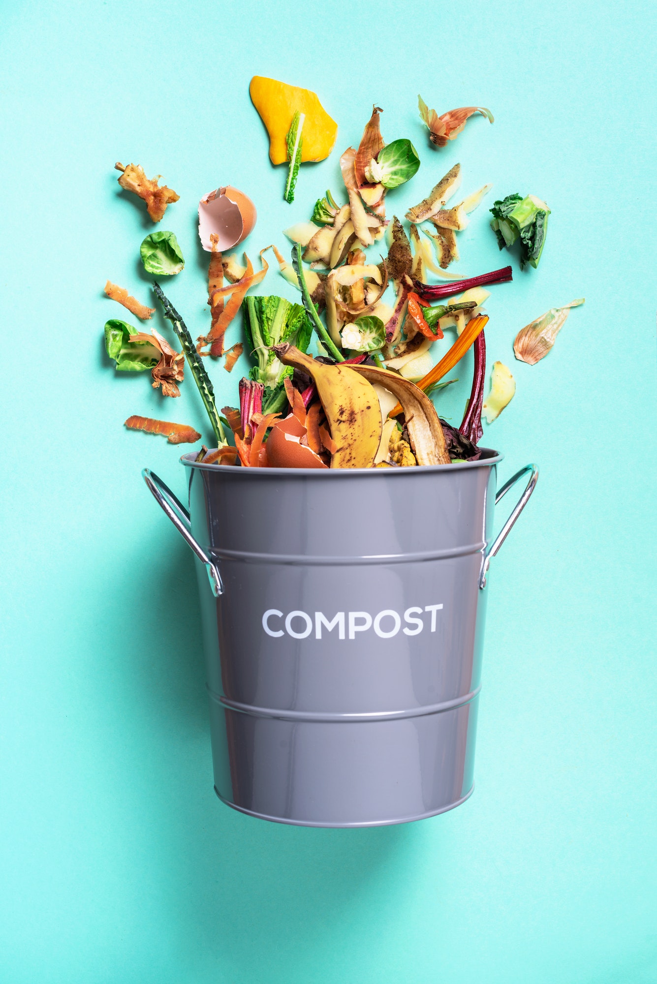 Peeled vegetables in white compost bin on blue background. Trash bin for composting with leftover